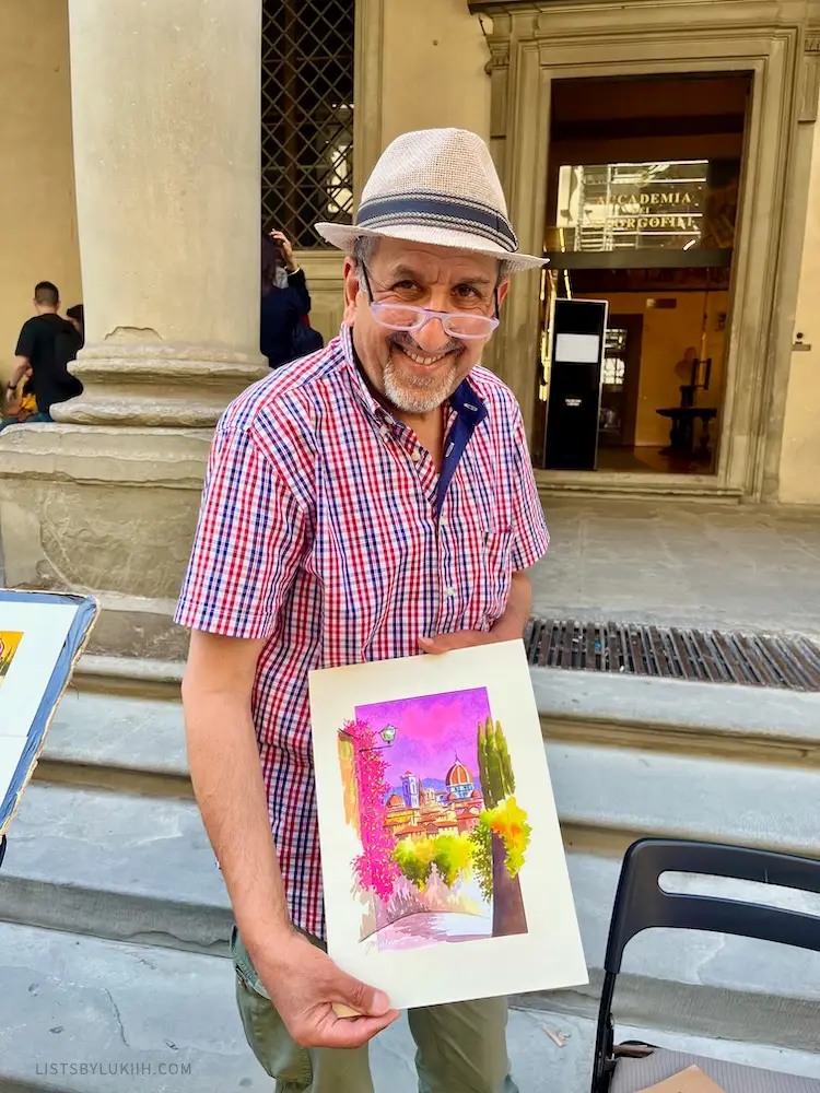 A man holding a watercolor painting outside in the streets.