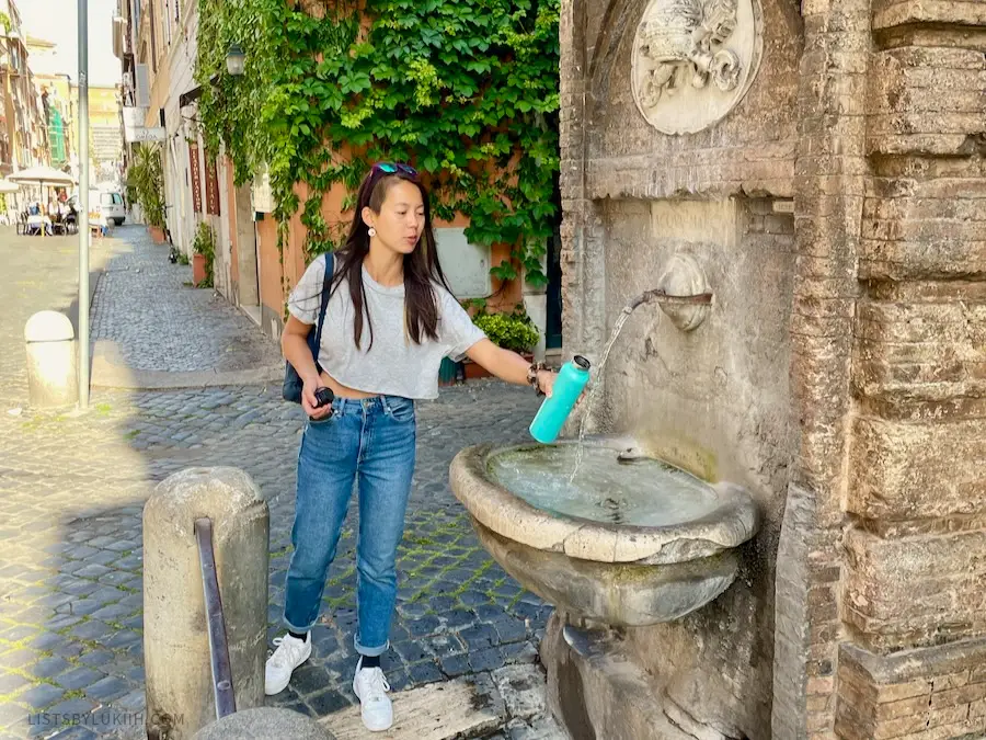 A woman holding out her water bottle in front of a decorated water fountain.