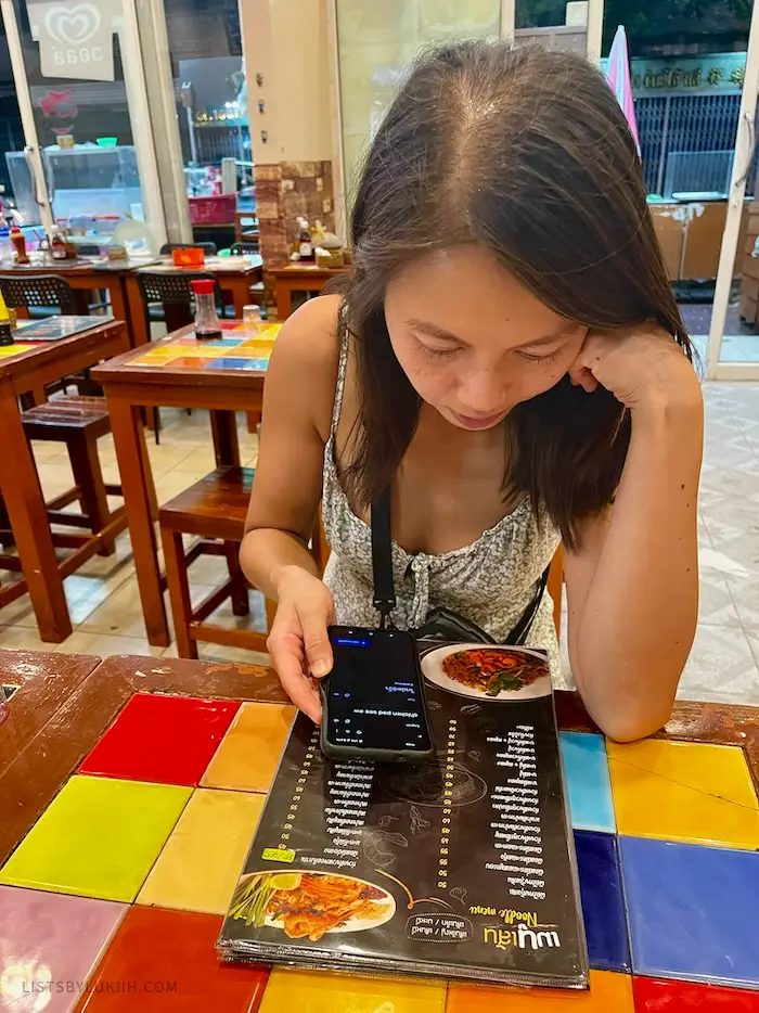 A woman looking at a menu in Thai while holding a phone.