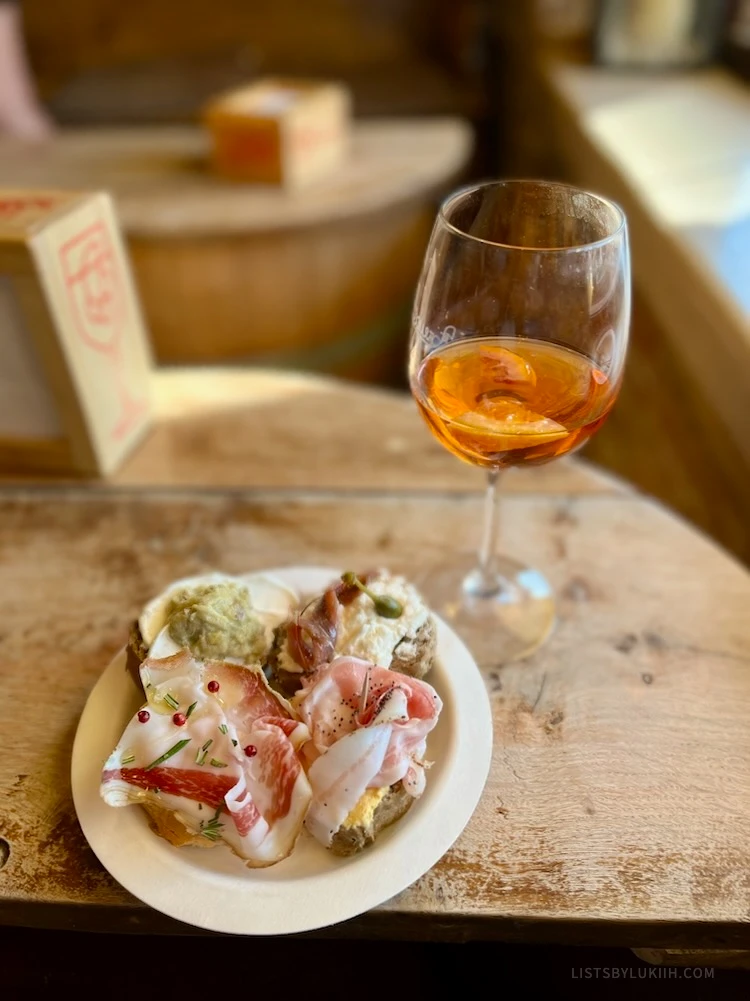 A plate of bread with different cured ham toppings and a wine glass with red-orange liquid.