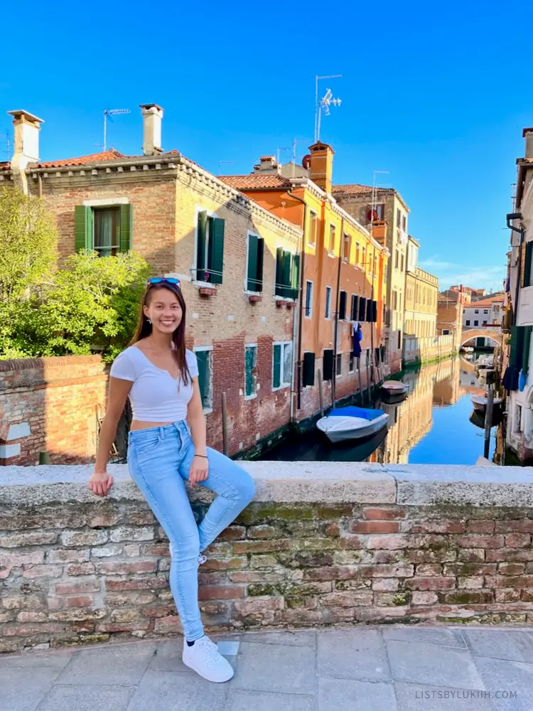 A woman sitting on a ledge overlooking a small canal.