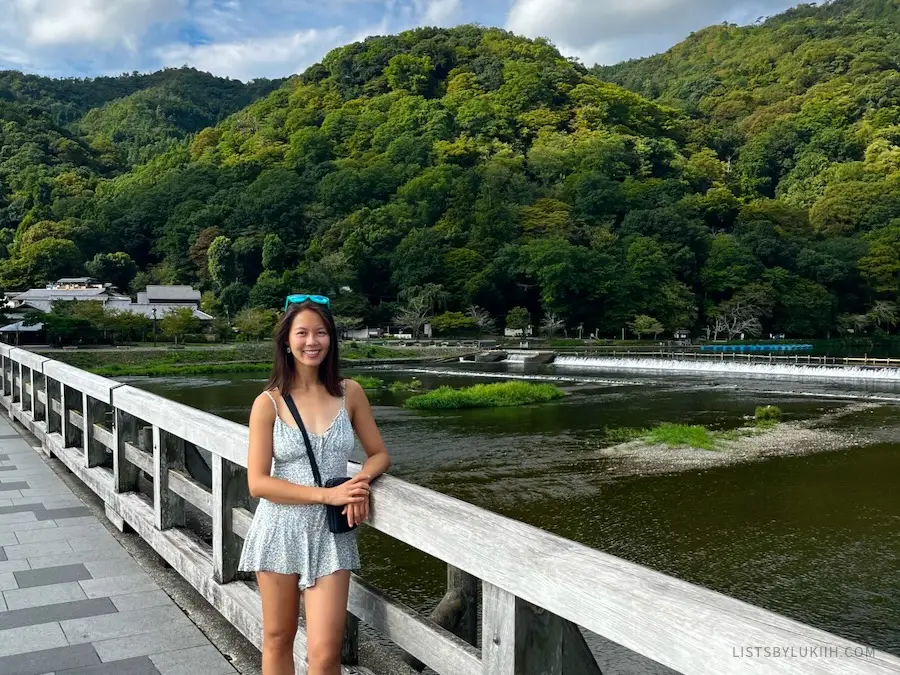 A woman standing on a bridge with a lush mountain background.
