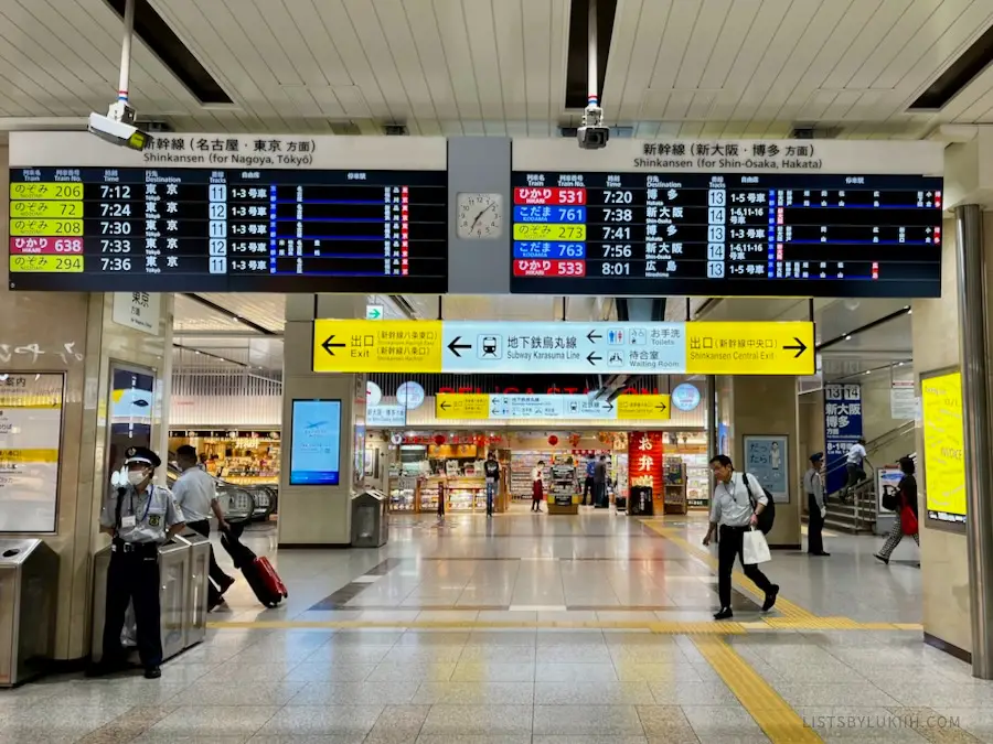 A clean metro station with digital time tables with stores in the background.