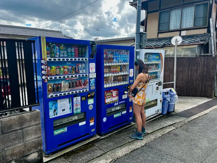 A woman standing in front of a set of vending machines selling bottled drinks.