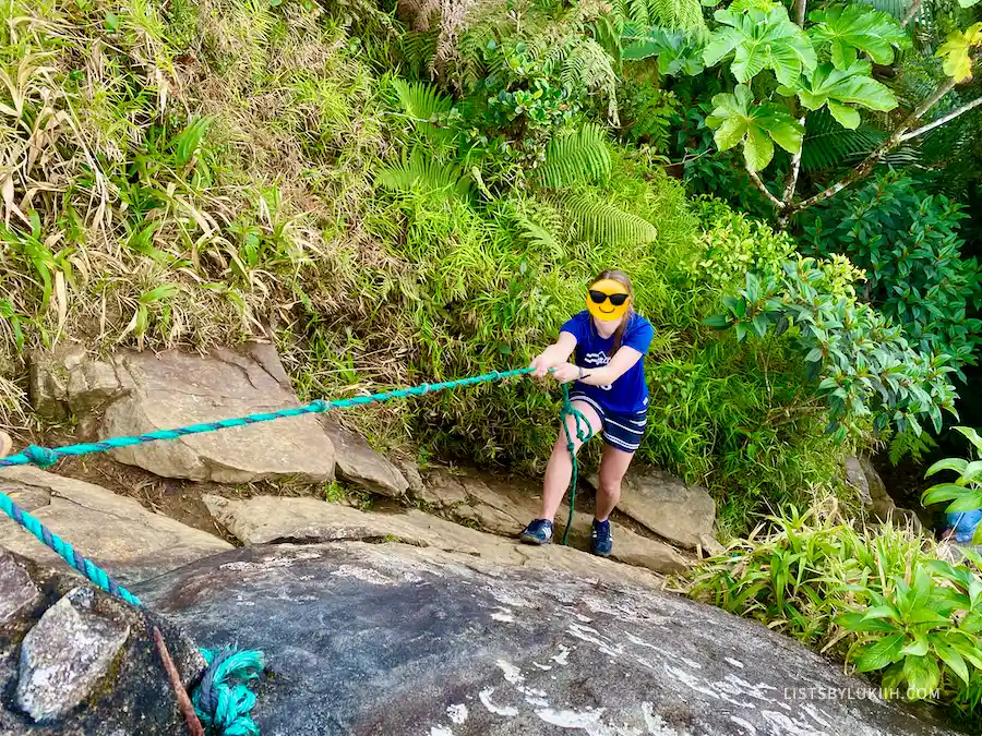 A woman climbing up a rock while holding a rope tied to the rocks.