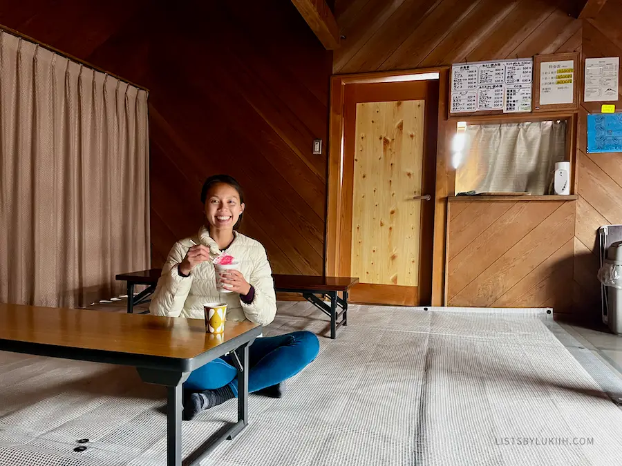 A woman sitting down in a Japanese hut with a cup noodle soup.