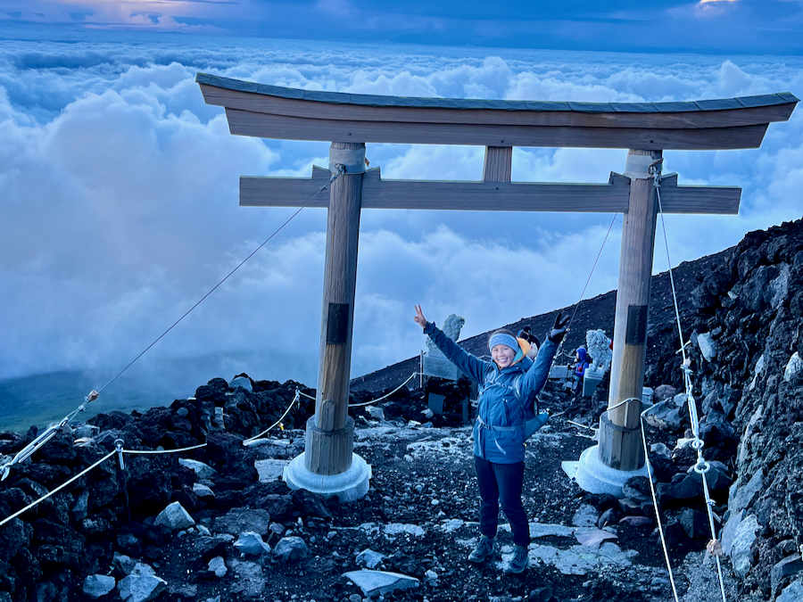 A hiker standing in front of a shrine overlooking clouds on a mountain.