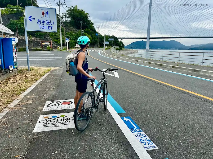 A woman holding a bike next to a blue line and sign that says Toilet.