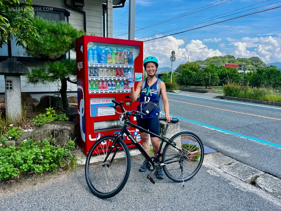 A woman with a bike standing next to a vending machine by the side of the road.
