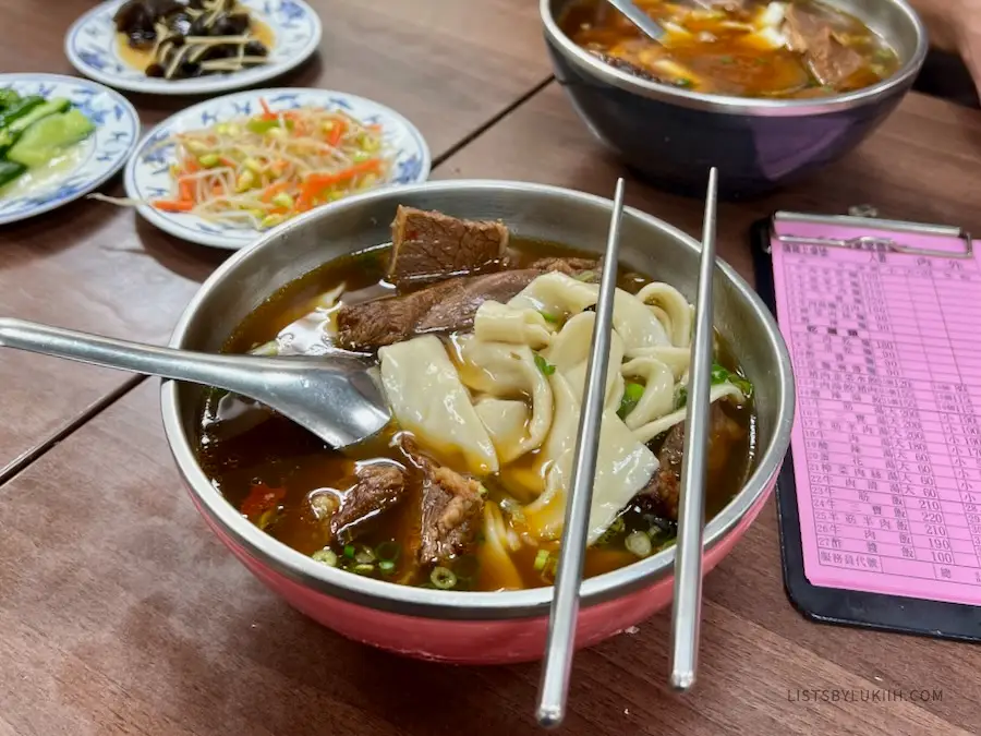 A bowl with thick noodles in a broth with beef.