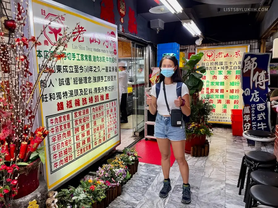A woman wearing shorts and a t shirt next to a sign with Chinese writing on it.