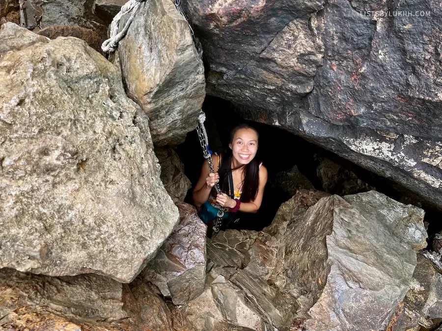A woman holding onto a metal chain climbing out of a cave surrounded by rocks.
