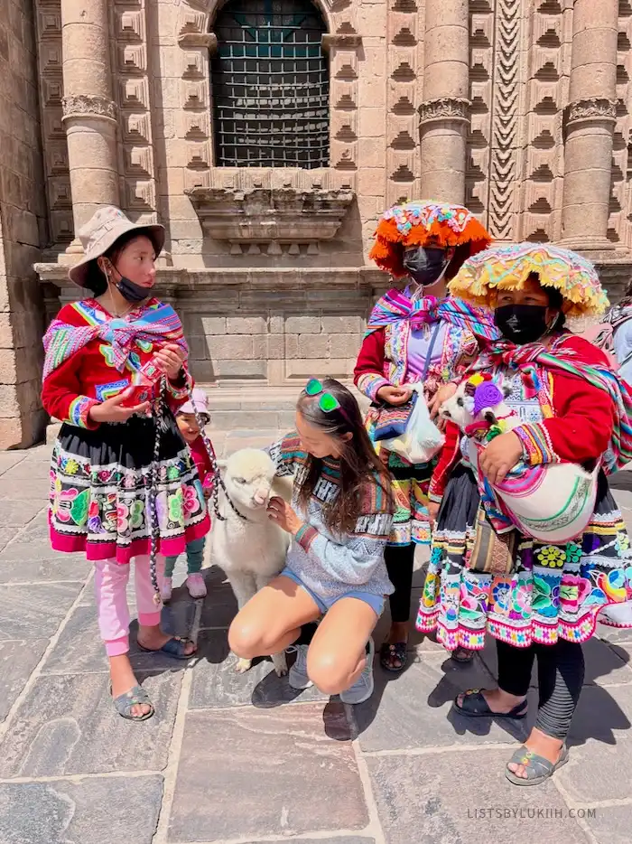 A tourist taking a photo with a baby alpaca and three women dressed in traditional Peruvian clothes.