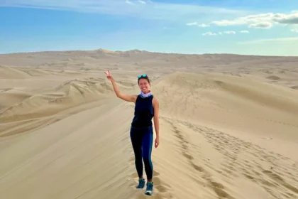 A woman standing on top of a sand dune and surrounded by desert.