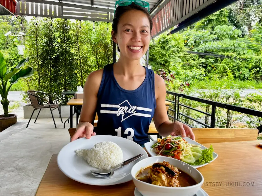 A woman holding a plate of salad, rice and curry with chicken in an outdoor area.