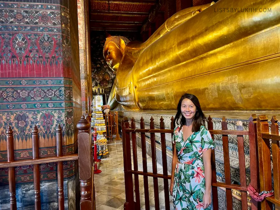 A woman standing in front of a giant gold statue resembling Buddha.