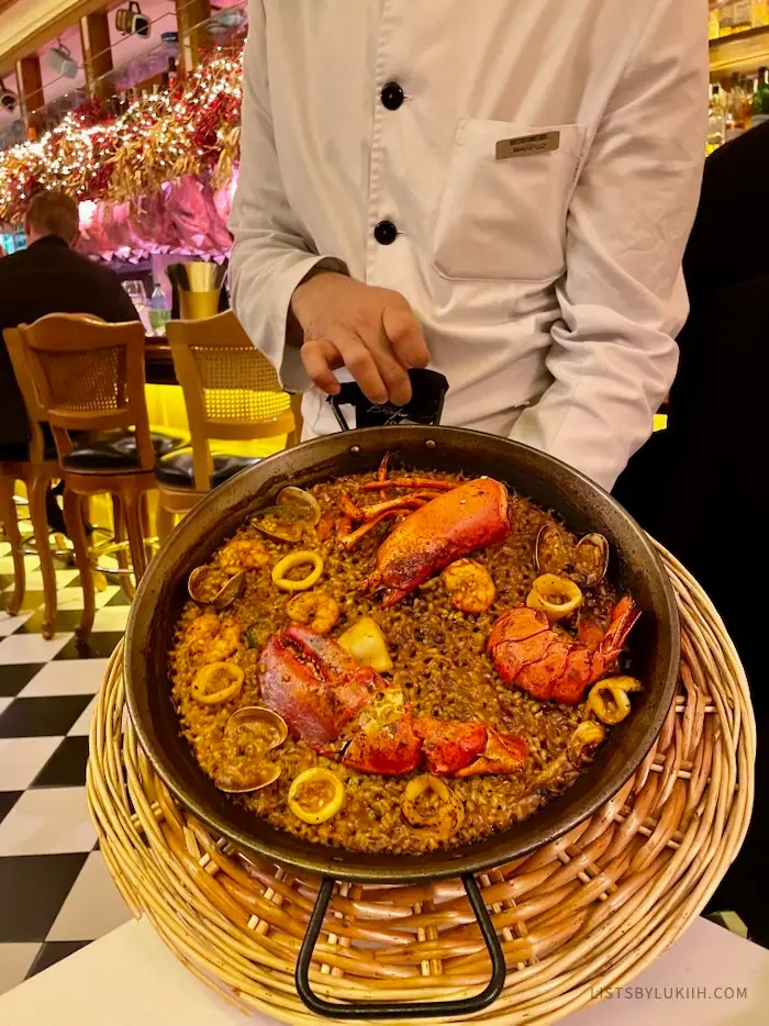A waiter holding a large pan with rice and lobster in it.