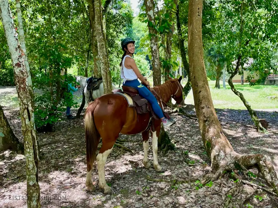 A woman riding a brown horse that's standing in between trees.