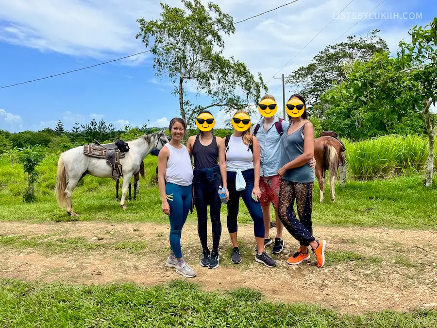A group of five people in athletic clothing and running shoes with horses in the background.