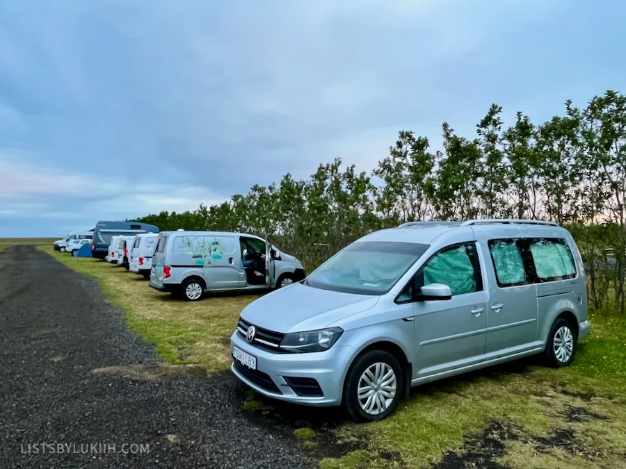 A row of campervans parked on a patch of grass outside while the sky is dim.