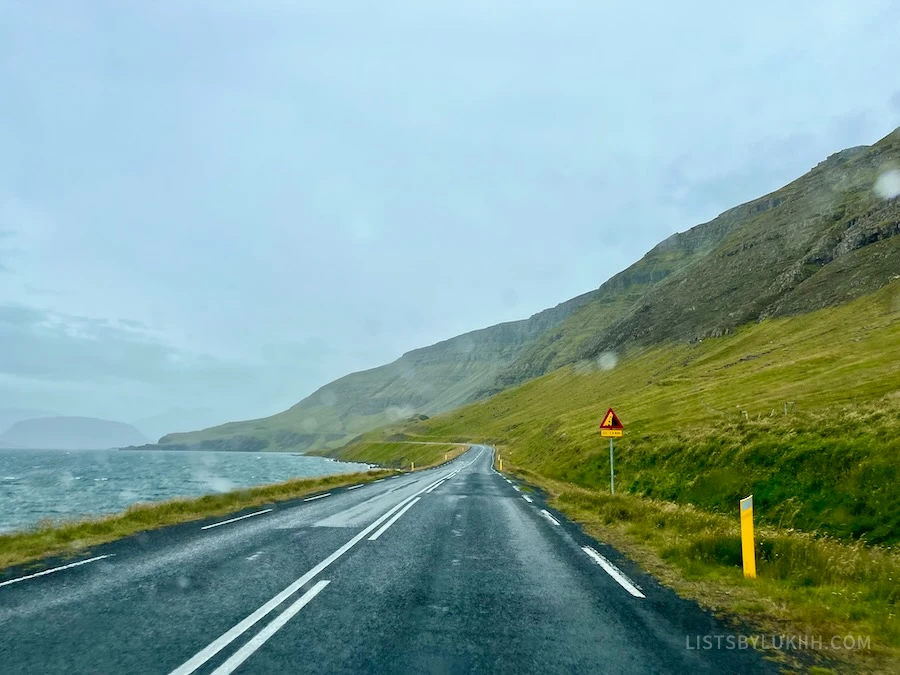 A road winding through mountains through a vehicle's rainy and wet windshield.