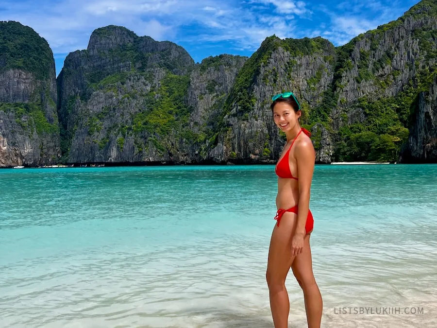 A woman standing in front of a blue ocean with limestone cliffs in the background.