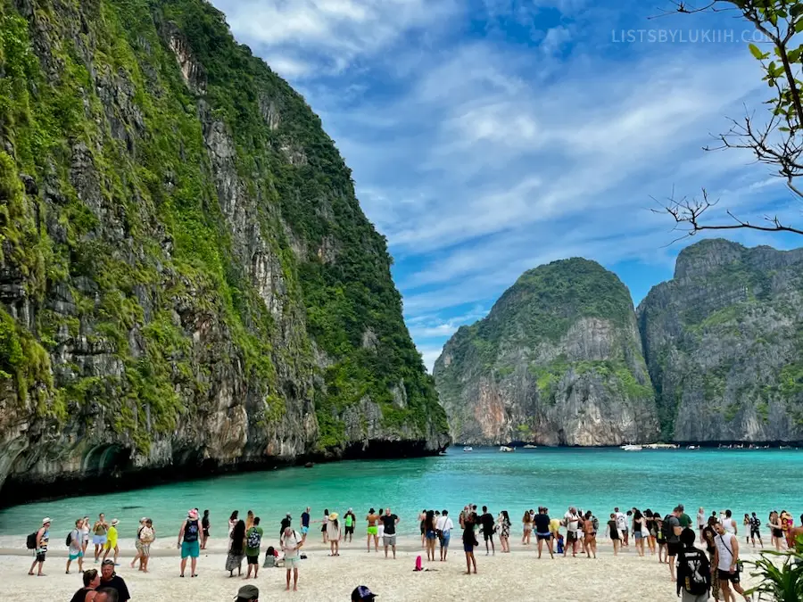 A blue ocean with white sand beach lined with people. Limestone cliffs surround the ocean.