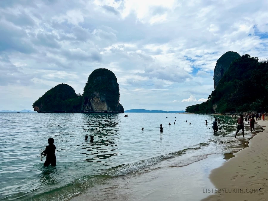 A beach with people in it and limestone cliffs in the background.