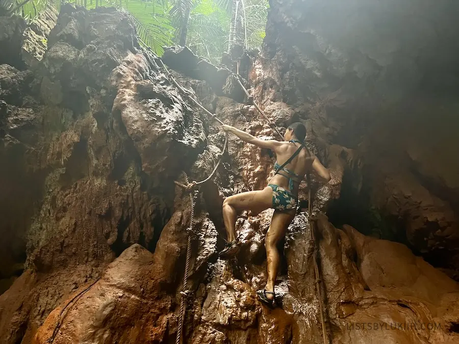 A woman holding ropes climbing up muddy, wet rocks.