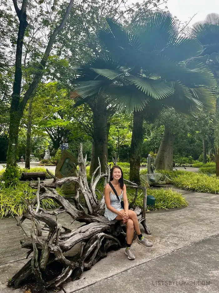 A woman sitting on a unique wooden chair at a park.