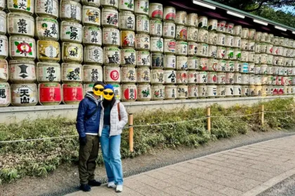 A couple standing in front of a wall with colorful barrels with Japanese writings.