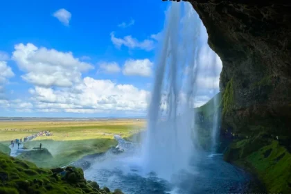 A big waterfall falling out of a cave during a sunny day.