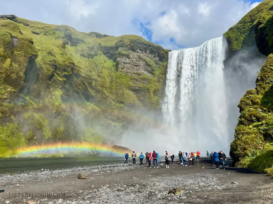 A big waterfall falling from a mountain next to two double rainbows.