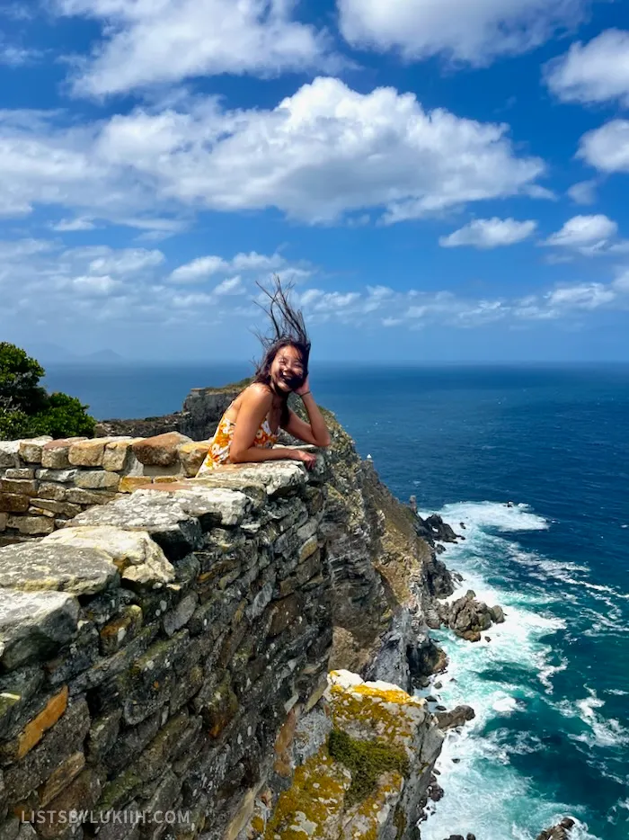A woman hunching over a stone ledge overlooking a blue ocean.