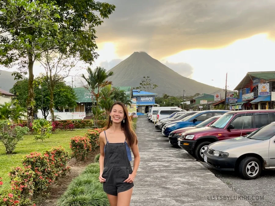 A woman standing in a street with the silhouette of a volcano in the background.