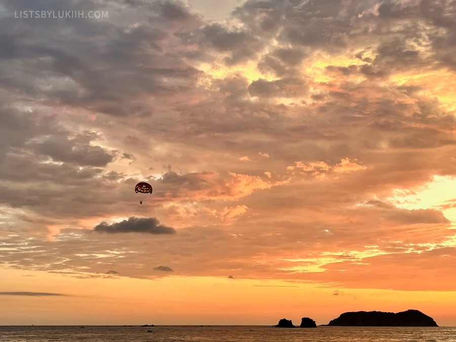 A deep-orange sunset with the ocean beneath and a person parasailing.