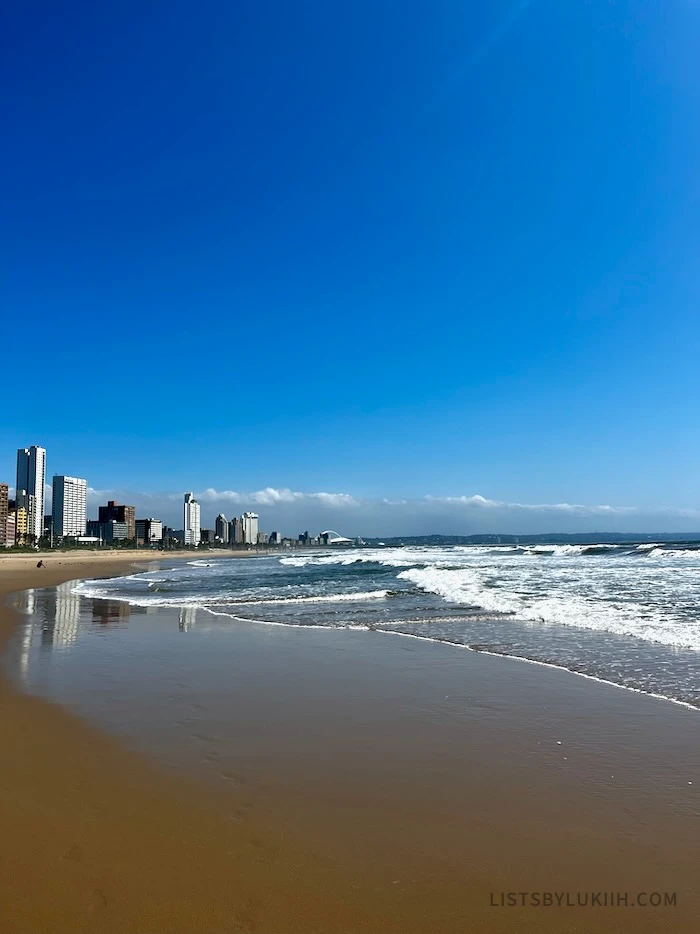A soft, sandy beach with tall buildings in the horizon.