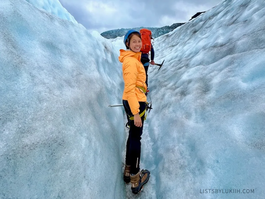 A woman wearing crampons in between two glaciers taller than her.