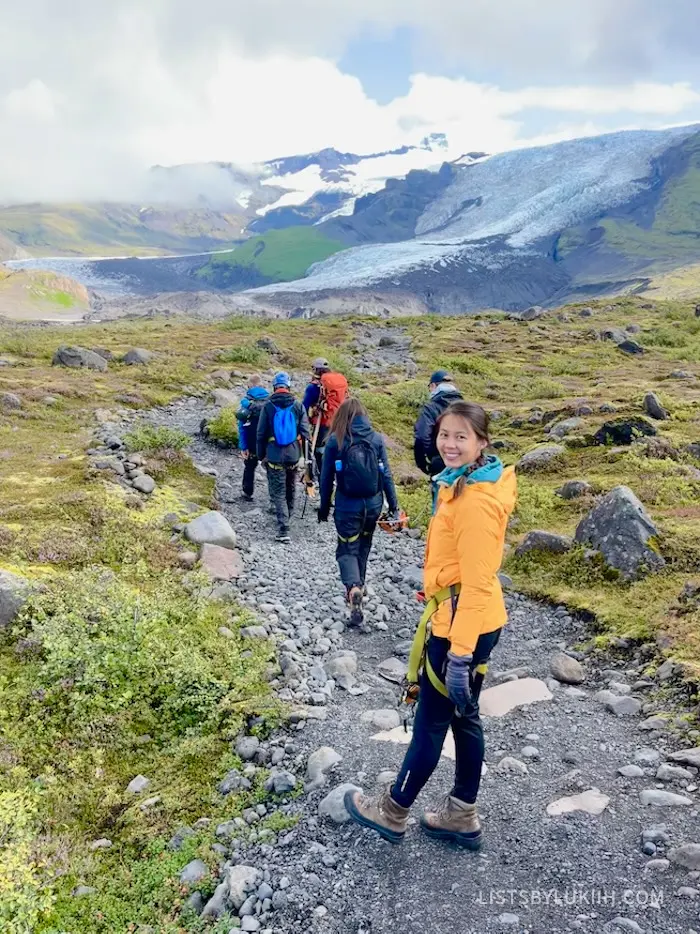 Six people walking on a trail towards a mountain with glacier on it.