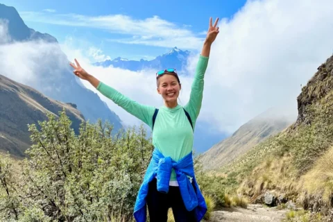 A woman throwing up peace-signs against a mountain background.