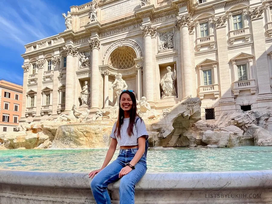 A woman sitting in front of a fountain surrounded by marble sculptures.