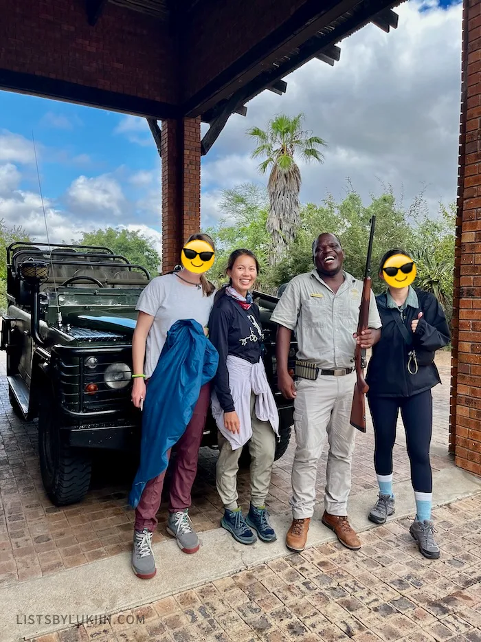 A group of people standing in front of an open vehicle with a safari guide holding a rifle for precaution.