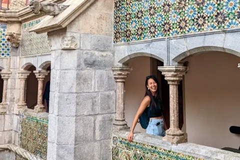 A woman peaking out of a castle's colorful arches.