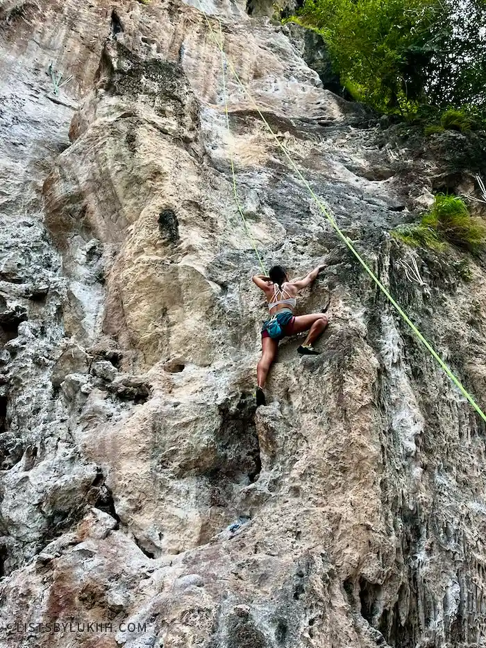 A woman climbing up a wall of rocks with a rope tied to her.