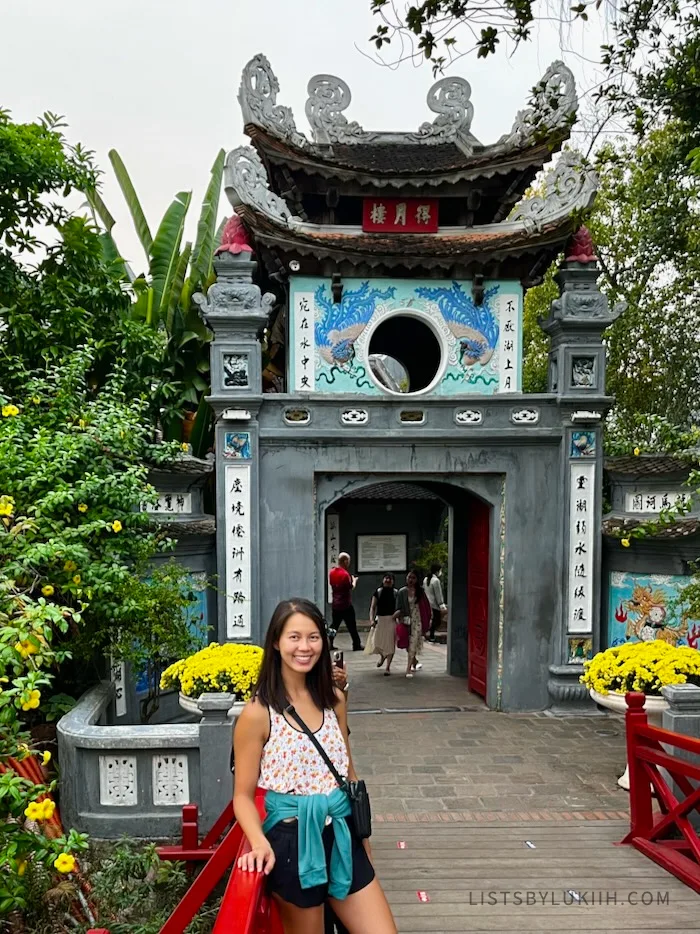 A woman standing on a bridge in front a decorated Asian gate.