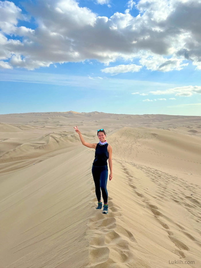 A woman standing on top of a sand dune and surrounded by desert.