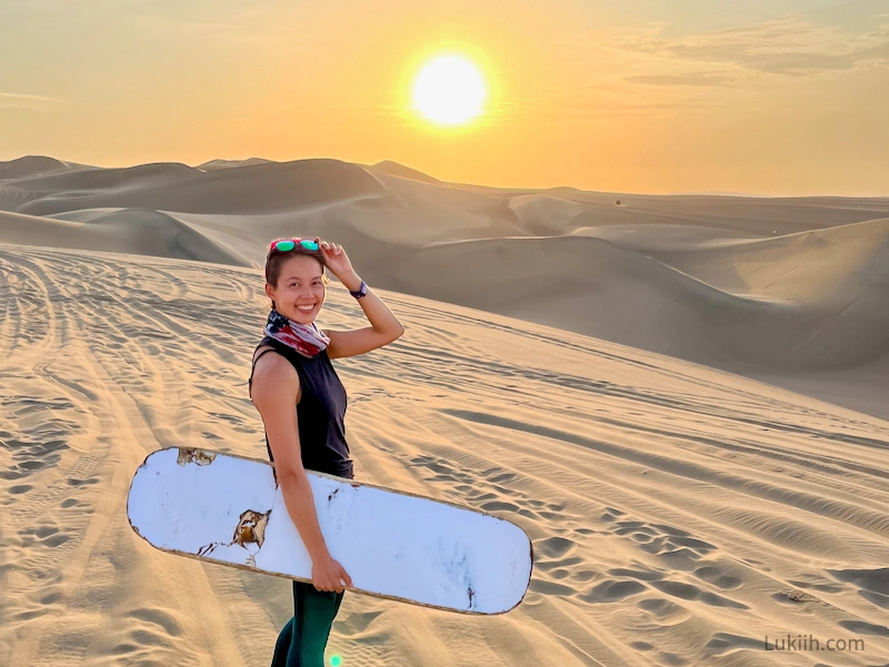 A woman standing in a desert holding a sand board.
