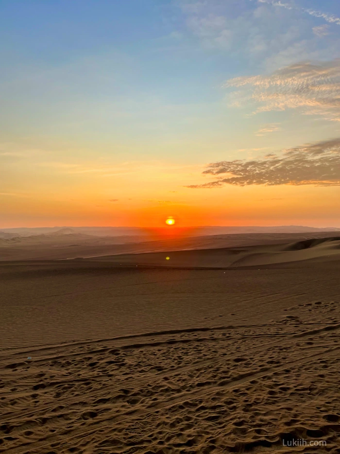A sun setting over a vast desert with sand dunes.