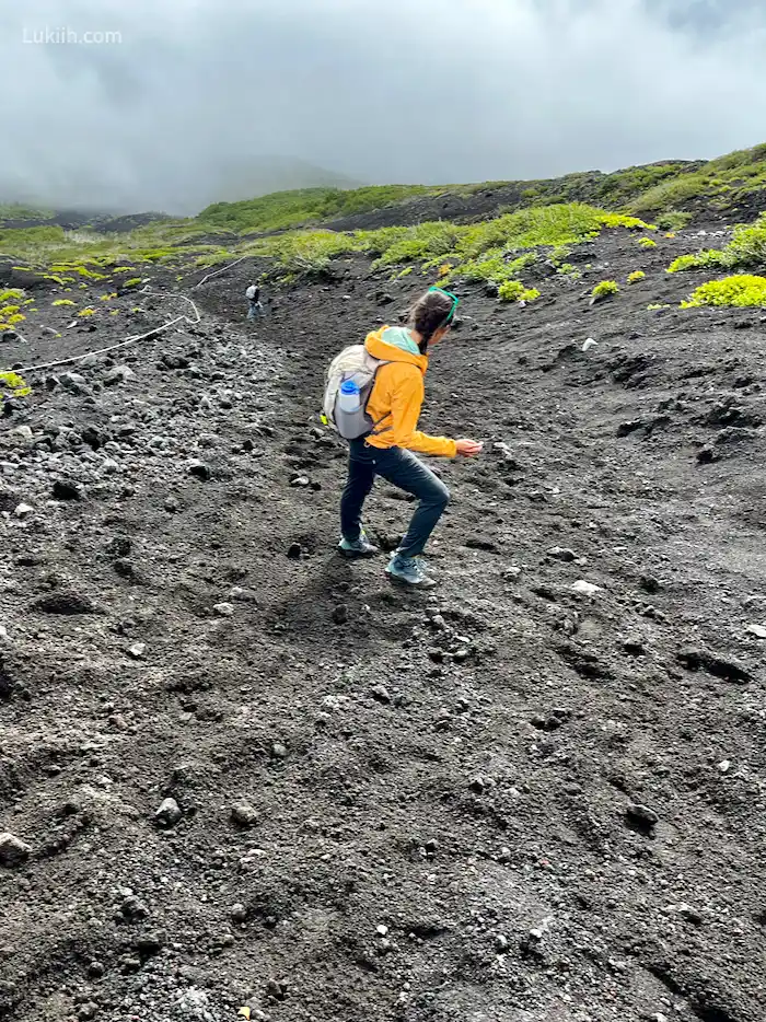 A hiker going down steep volcanic gravel.