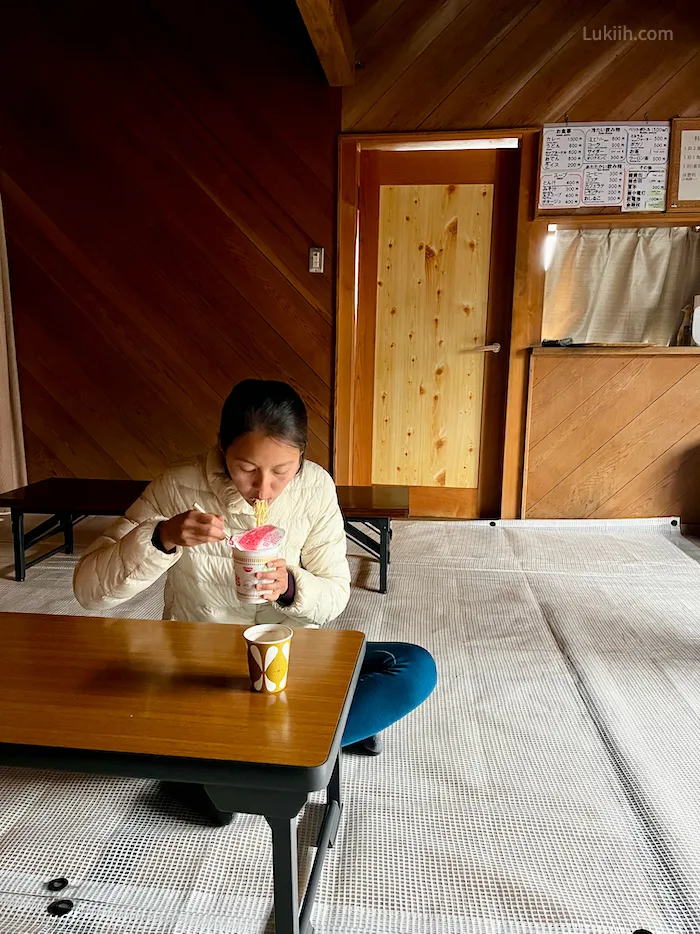 A woman sitting in a simple hut eating ramen.